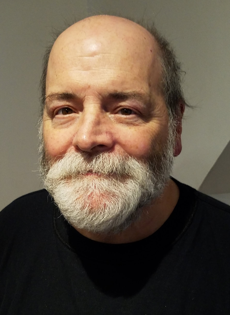 Photo of Tony Ferreira, a white man with brown eyes, salt-and-pepper hair in a tonsure around his head, and a full salt-and-pepper beard and sideburns, looking directly at the camera with a smile. Only his head and shoulders are visible against a white background. He is wearing a black shirt with a crew neckline.
